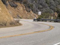 there is a sign posted to the side of a curved road near some hills or bushes