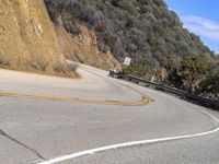 there is a sign posted to the side of a curved road near some hills or bushes