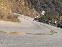 there is a sign posted to the side of a curved road near some hills or bushes