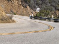 there is a sign posted to the side of a curved road near some hills or bushes