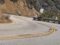 there is a sign posted to the side of a curved road near some hills or bushes