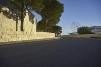 a curved road leads up to a wall lined with trees and sculptures in front of the building