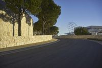 a curved road leads up to a wall lined with trees and sculptures in front of the building