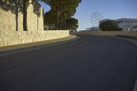 a curved road leads up to a wall lined with trees and sculptures in front of the building