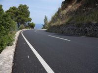 the road curves through an area of rock and trees with sea in the distance and blue sky
