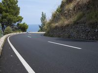 the road curves through an area of rock and trees with sea in the distance and blue sky