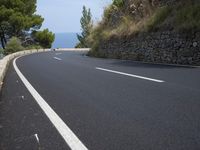 the road curves through an area of rock and trees with sea in the distance and blue sky