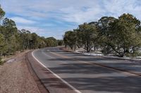 a curve in the road with trees on either side and snow on both sides and two lanes in the middle