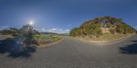 a curved road going to a grassy field near the ocean and hills with sunbeams