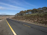 the back end of a long curved road in the middle of a hilly field near an open sky