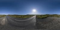 a long curved road curves through the desert with the sun shining above it as well as grass