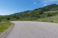 a curved road running through the mountains with vegetation on both sides and a blue sky overhead