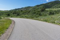 a curved road running through the mountains with vegetation on both sides and a blue sky overhead