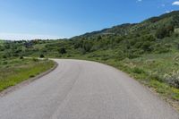 a curved road running through the mountains with vegetation on both sides and a blue sky overhead