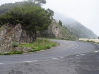 a curved road with no cars on the side of it, in front of a cliff