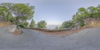 a very long curved road with a stone fence and some trees near it by the ocean