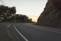 a curved roadway going next to the mountain side with power lines above it and telephone poles on the other side