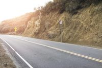 a curved roadway going next to the mountain side with power lines above it and telephone poles on the other side