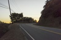 a curved roadway going next to the mountain side with power lines above it and telephone poles on the other side