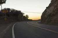 a curved roadway going next to the mountain side with power lines above it and telephone poles on the other side