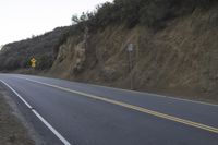 a curved roadway going next to the mountain side with power lines above it and telephone poles on the other side