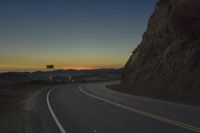 a curved roadway going next to the mountain side with power lines above it and telephone poles on the other side