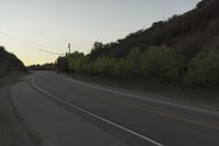 a curved roadway going next to the mountain side with power lines above it and telephone poles on the other side