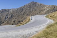 a curved road going up to a mountain side with a person on the front motorcycle and in the rear seat