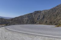 a curved road on the side of a mountain road in the middle of it are three sides are steep mountains