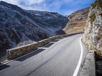 a curved road runs up the side of a mountain range in italy with snowy mountains