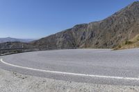 a curved road next to a mountainous mountain range with a guard rail on the left