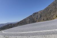 a curved road next to a mountainous mountain range with a guard rail on the left