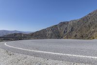 a curved road next to a mountainous mountain range with a guard rail on the left