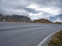 an empty road leads through the mountains and hills to a building on the right with a wind farm in the distance