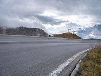 an empty road leads through the mountains and hills to a building on the right with a wind farm in the distance