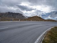 an empty road leads through the mountains and hills to a building on the right with a wind farm in the distance