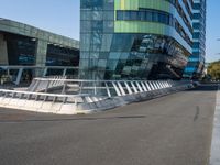 a curved road near a building with large windows on it's sides and green and blue facade