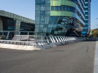 a curved road near a building with large windows on it's sides and green and blue facade