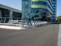 a curved road near a building with large windows on it's sides and green and blue facade