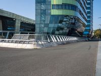 a curved road near a building with large windows on it's sides and green and blue facade