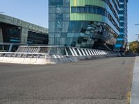 a curved road near a building with large windows on it's sides and green and blue facade