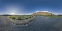 a wide angle image of a curved road with a very large mountain in the background