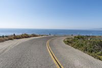 a curved road on the side of the road that leads to the ocean in front of it