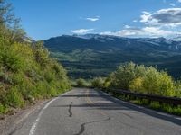 a person on a long stretch of road next to a mountain range under blue skies