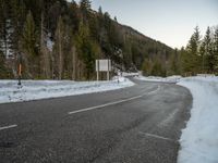 a curved road surrounded by snow covered evergreen trees in the sun light of day, as seen from behind