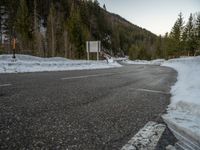 a curved road surrounded by snow covered evergreen trees in the sun light of day, as seen from behind