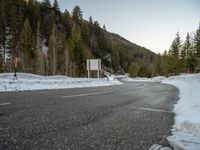 a curved road surrounded by snow covered evergreen trees in the sun light of day, as seen from behind