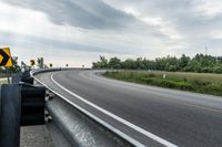 a curved road with signs on the roadsides in front of the sky with clouds and green grass