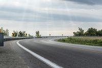 a curved road with signs on the roadsides in front of the sky with clouds and green grass