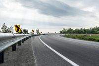 a curved road with signs on the roadsides in front of the sky with clouds and green grass